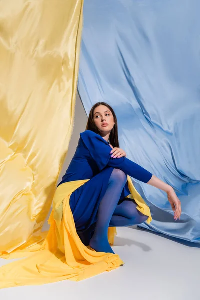 Trendy young ukrainian woman in stylish color block clothing sitting near blue and yellow flag — Stockfoto