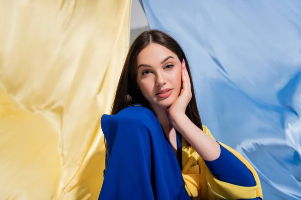 Pretty ukrainian woman in stylish color block clothing posing near blue and yellow flag - foto de stock