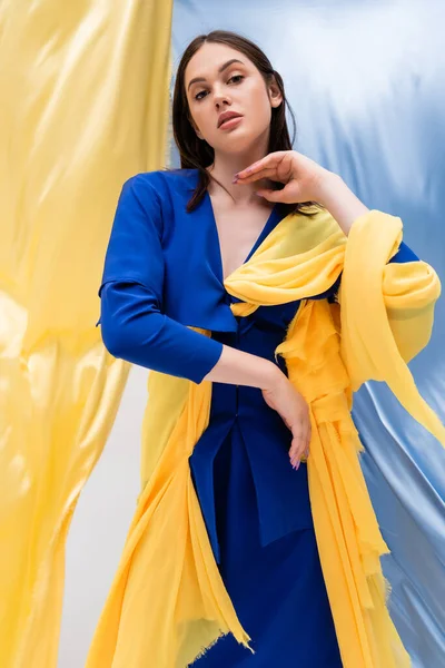 Ukrainian young woman in stylish color block clothing posing near blue and yellow fabric — Stock Photo