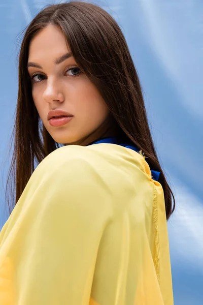 Portrait of pretty ukrainian woman in yellow clothing looking at camera near blue fabric — Stockfoto