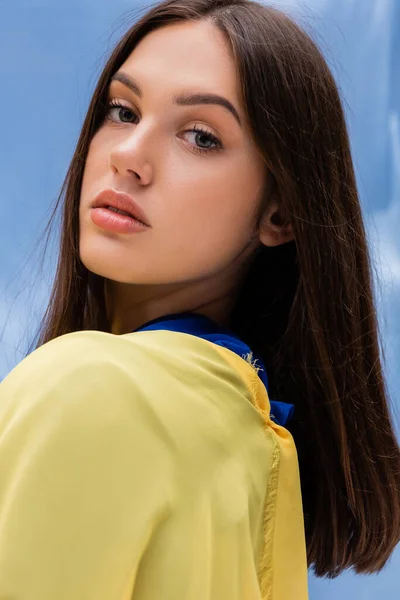 Portrait de jeune femme ukrainienne en vêtements jaunes regardant la caméra près du tissu bleu — Photo de stock