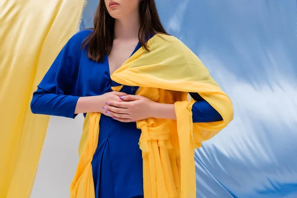Vue recadrée de la jeune femme ukrainienne patriotique dans des vêtements élégants posant près de tissu bleu et jaune — Photo de stock