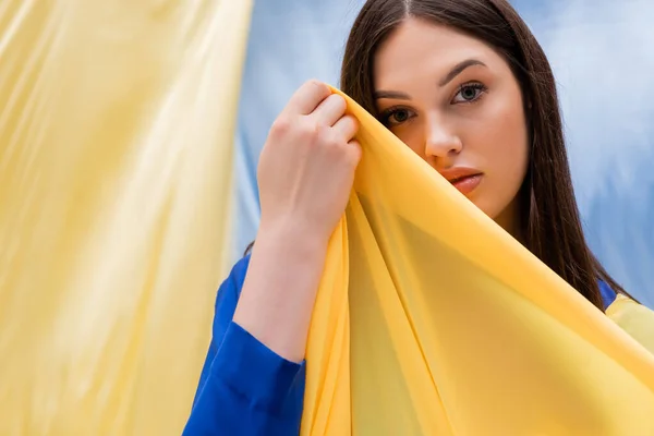 Patriottica ucraina giovane donna che tiene drappeggio vicino bandiera blu e gialla — Foto stock