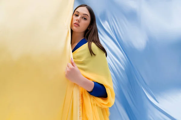 Patriotic ukrainian woman in clothing posing near blue and yellow flag - foto de stock