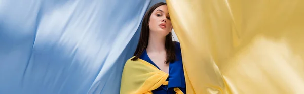 Патриотическая украинская молодая женщина в модной одежде позирует рядом с сине-желтой тканью, баннером — стоковое фото