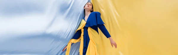 Patriotic ukrainian woman in fashionable outfit posing near blue and yellow fabric, banner — Stockfoto