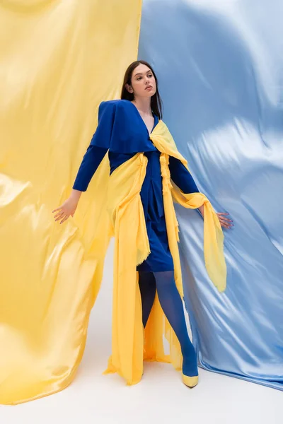 Longitud completa del modelo patriótico ucraniano en traje elegante posando cerca de tela azul y amarillo - foto de stock