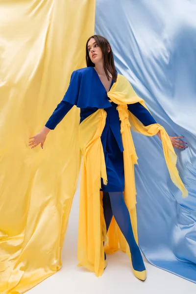 Longitud completa del modelo patriótico ucraniano en traje de moda posando cerca de tela azul y amarillo - foto de stock