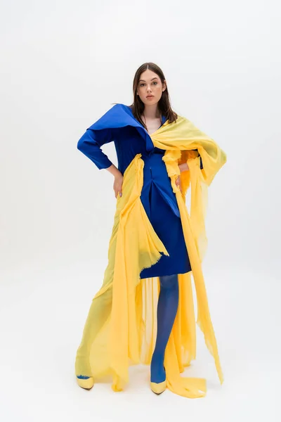 Full length of confident ukrainian woman in blue and yellow outfit posing with hands on hips on grey - foto de stock
