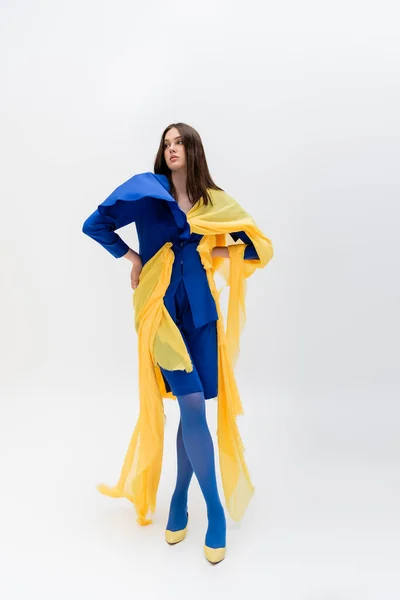 Full length of confident ukrainian woman in blue and yellow clothes posing with hands on hips on grey - foto de stock