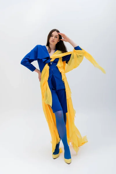 Piena lunghezza di donna ucraina fiduciosa in abiti blu e gialli in posa con mano sul fianco su grigio — Foto stock