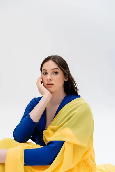 Bonita mujer joven ucraniana en traje azul y amarillo mirando a la cámara aislada en gris - foto de stock