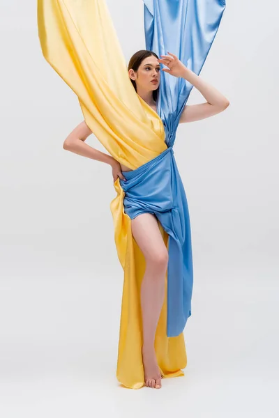 Jeune femme ukrainienne en robe bleue et jaune posant à la main sur la hanche sur gris — Photo de stock