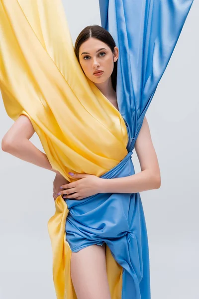 Young ukrainian woman in trendy blue and yellow dress posing with hand on hip isolated on grey — Stock Photo