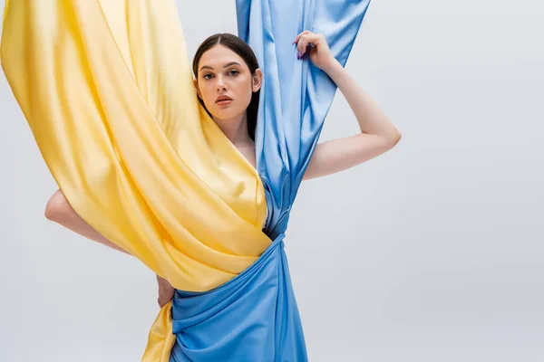 Bonita mujer ucraniana en vestido azul y amarillo posando con la mano en la cadera aislada en gris - foto de stock