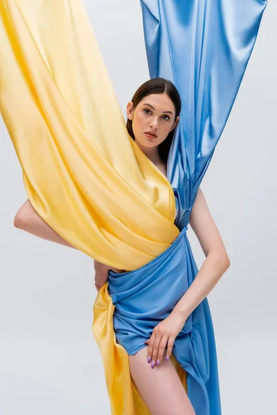 Pretty woman in ukrainian blue and yellow dress posing with hand on hip isolated on grey — Photo de stock