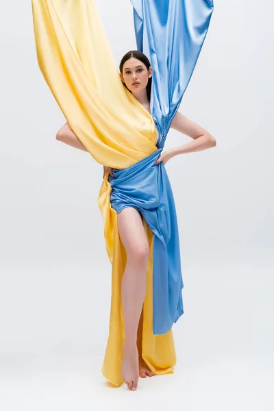 Pleine longueur de jolie femme en robe bleue et jaune ukrainienne posant avec les mains sur les hanches sur gris — Photo de stock