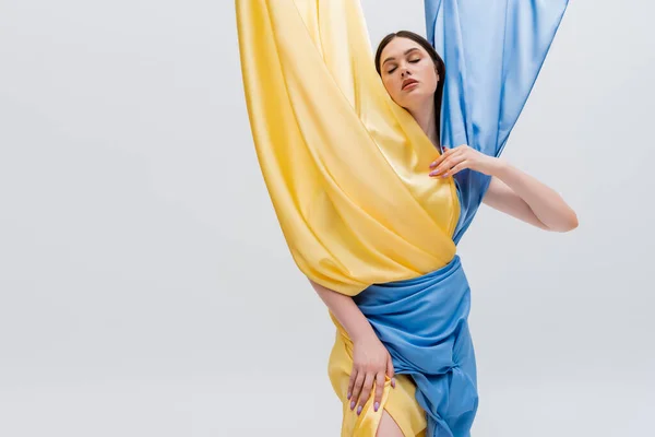 Young brunette woman in blue and yellow dress posing with closed eyes isolated on grey — Stock Photo