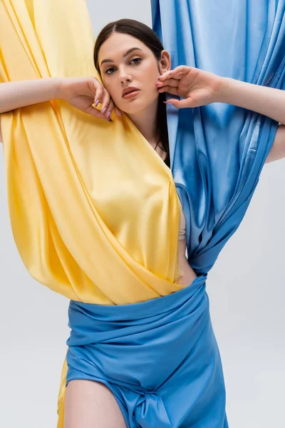 Jolie femme ukrainienne en robe bleue et jaune regardant la caméra isolée sur gris — Photo de stock