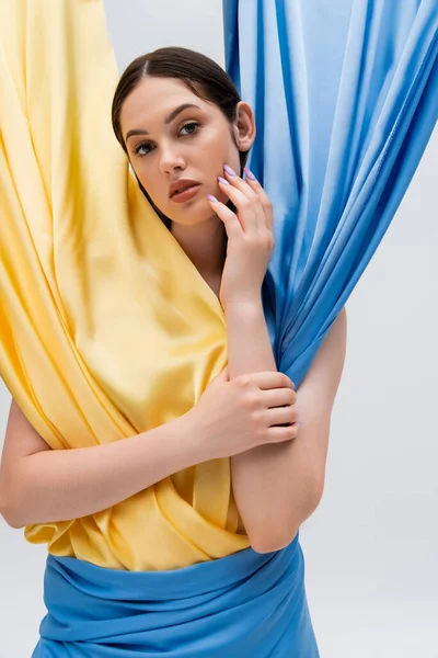 Pretty woman in ukrainian blue and yellow dress looking at camera isolated on grey — Foto stock