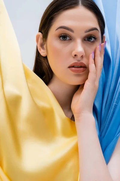 Portrait of pretty and young ukrainian woman near blue and yellow fabric isolated on grey — Stock Photo