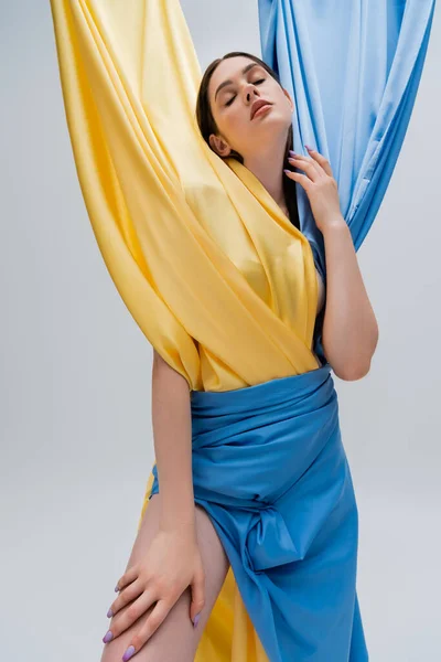 Pretty ukrainian woman with closed eyes in blue and yellow dress posing isolated on grey — Stockfoto