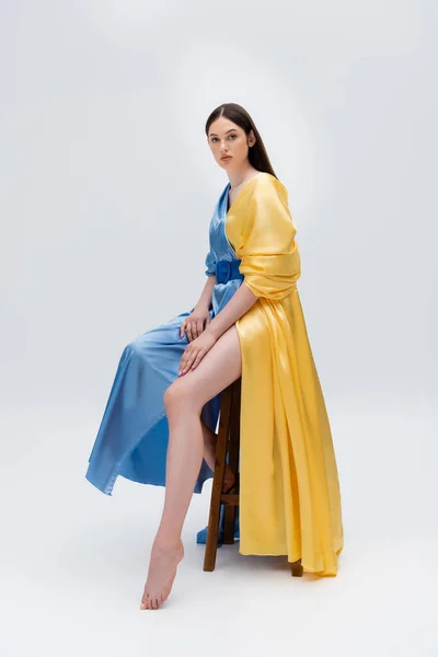 Повний зріст чуттєвої жінки в синьому і жовтому вбранні, сидячи на сірому — стокове фото
