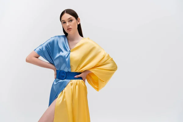 Brünette Ukrainerin in blau-gelbem Kleid posiert mit Händen auf Hüften isoliert auf grau — Stockfoto