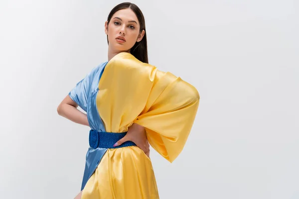 Sensual young ukrainian woman in blue and yellow dress posing with hands on hips and looking at camera isolated on grey — Stock Photo