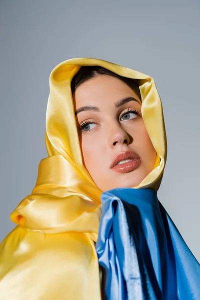 Young parotitic woman covered with ukrainian flag looking away isolated on grey — Photo de stock