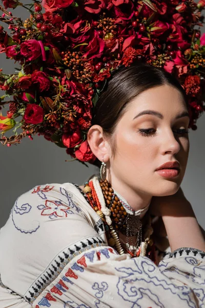 Portrait of pretty ukrainian woman in traditional clothes and floral wreath with red berries isolated on grey — Stockfoto