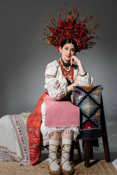 Thoughtful ukrainian woman in traditional clothes and red wreath with flowers and berries on grey — Photo de stock