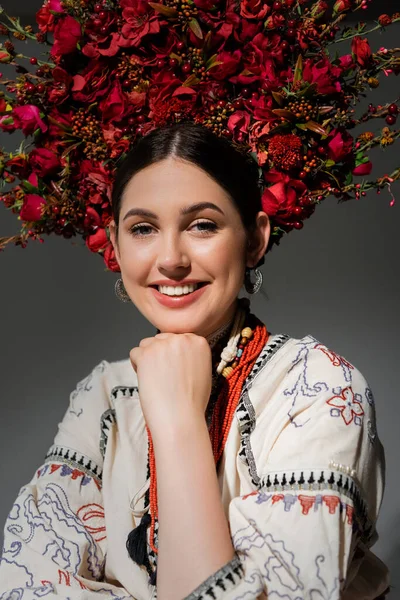 Retrato de mujer ucraniana sonriente en ropa tradicional y corona roja con flores y bayas aisladas en gris - foto de stock