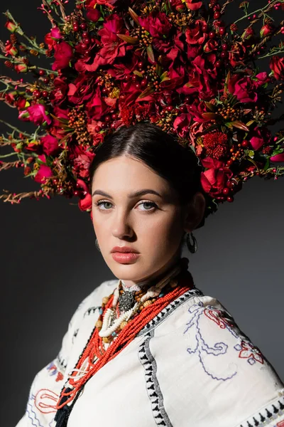 Portrait de jolie et jeune femme ukrainienne en couronne florale avec des baies rouges isolées sur gris foncé — Photo de stock