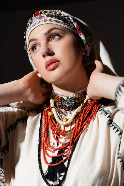 Portrait of ukrainian woman in traditional shirt with red ornament and headwear posing isolated on black — Photo de stock