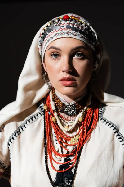 Portrait of ukrainian woman in traditional shirt with red ornament and headwear looking at camera isolated on black — Photo de stock