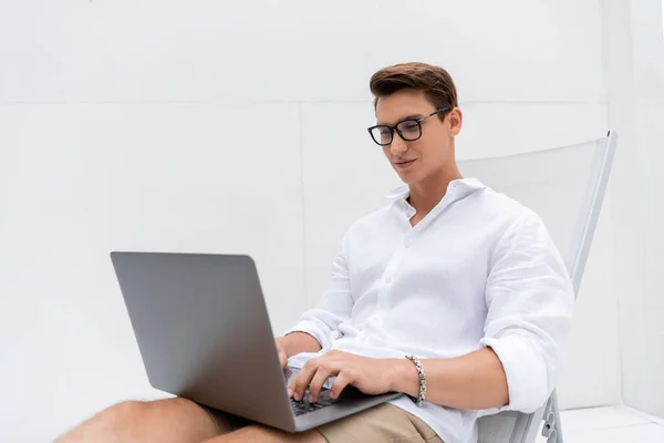 Positive man in eyeglasses typing on laptop in deck chair outdoors — Stock Photo