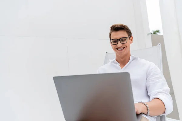 Happy man in eyeglasses using laptop in deck chair outdoors — Foto stock