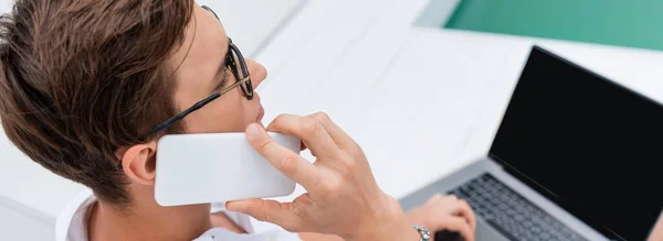 High angle view of man talking on smartphone near blurred laptop at poolside, banner — Stock Photo