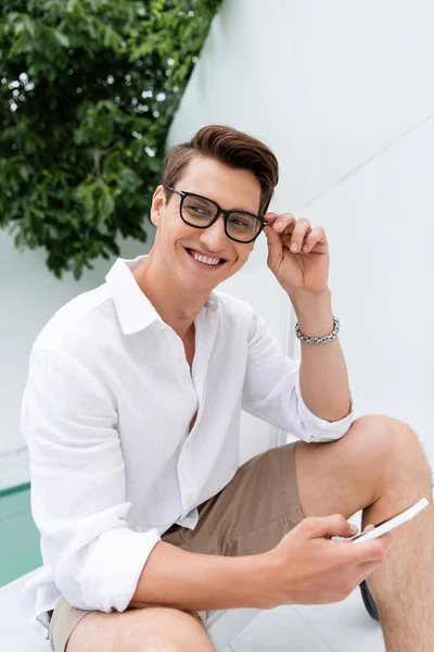 Happy man with mobile phone looking away while sitting at poolside — Stock Photo