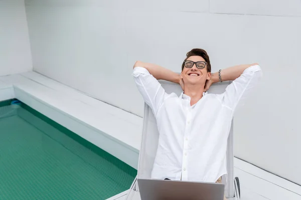 Glücklicher Mann mit Laptop entspannt im Liegestuhl am Pool — Stockfoto