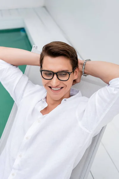 High angle view of smiling man in sunglasses sitting with hands behind head — Stock Photo