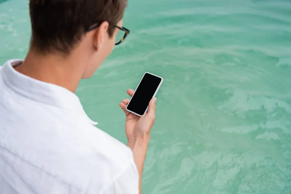 Чоловік тримає мобільний телефон з порожнім екраном біля басейну з бірюзовою водою — стокове фото