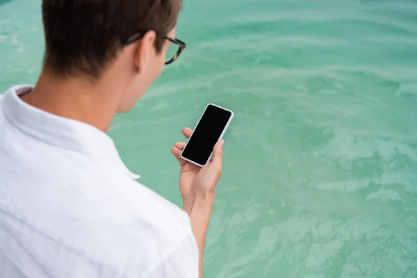 Man holding mobile phone with blank screen near pool with turquoise water — Stock Photo
