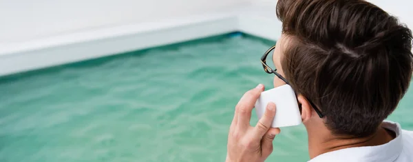 Man in eyeglasses calling on cellphone near pool, banner — стоковое фото