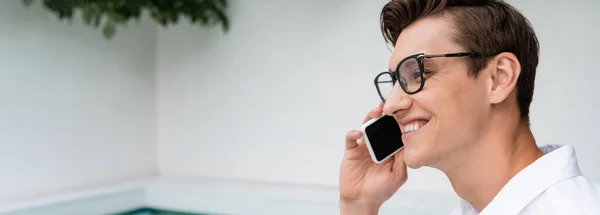 Uomo positivo in occhiali da vista sorridente mentre parla su smartphone all'aperto, banner — Foto stock