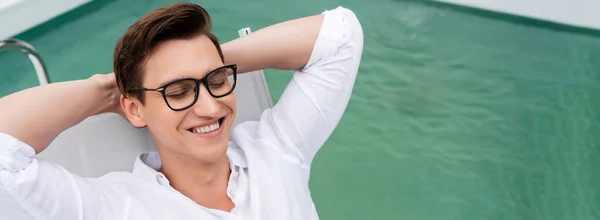 High angle view of happy man in eyeglasses relaxing with hands behind head at poolside, banner — Foto stock