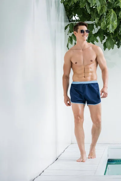 Full length of smiling sportive man walking along poolside by white wall - foto de stock