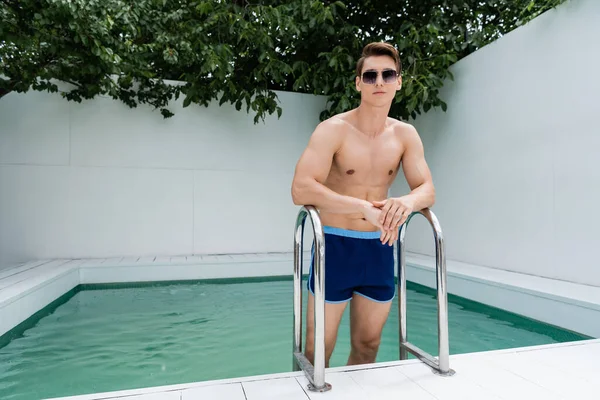 Людина в басейнах і сонцезахисних окулярах стоїть біля басейну драбини — стокове фото