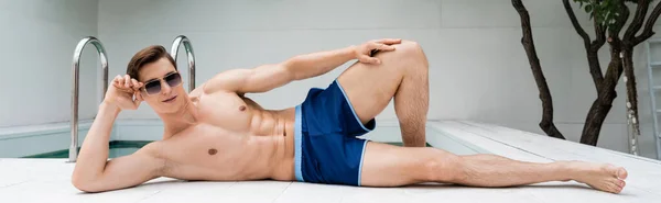 Full length of sportive man adjusting sunglasses while resting at poolside, banner — Stock Photo